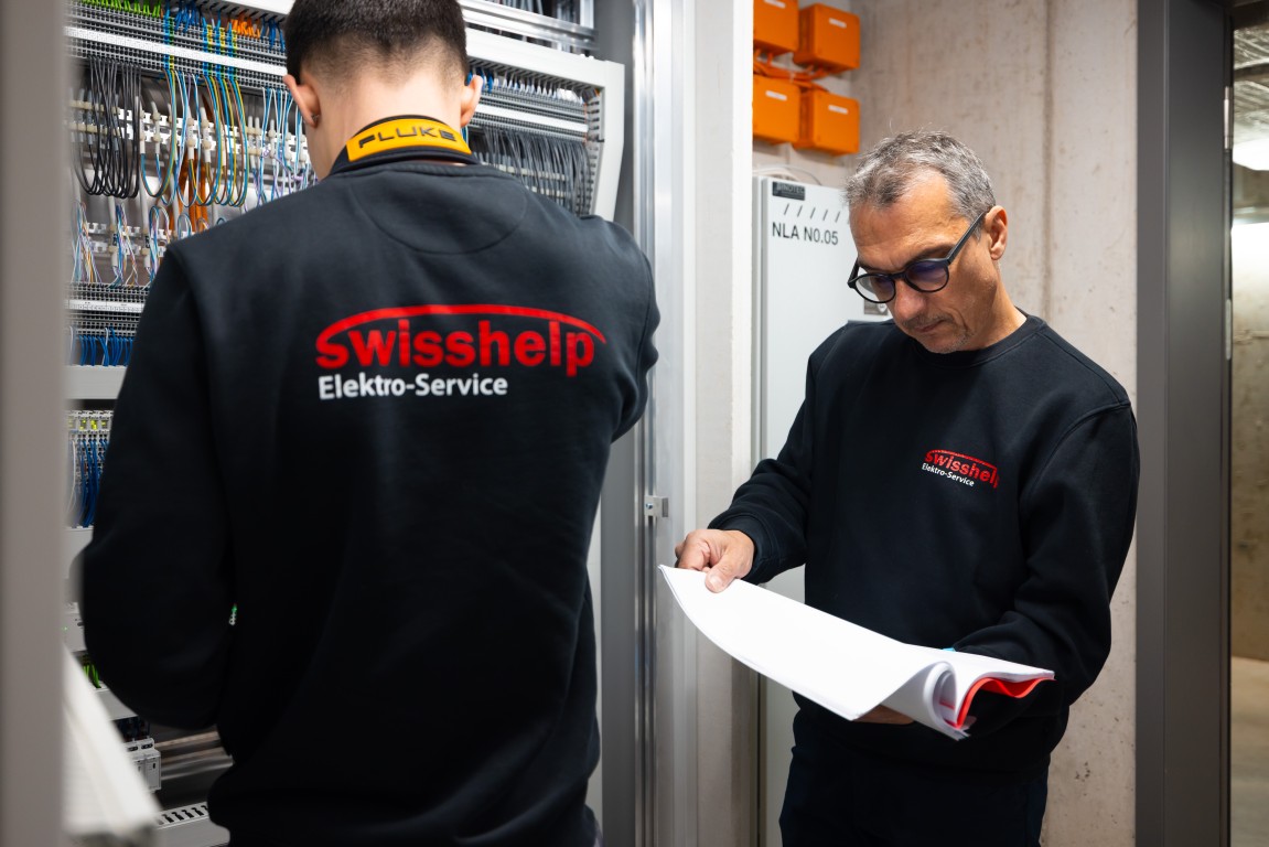 Zwei Swisshelp-Techniker prüfen einen Elektroverteiler