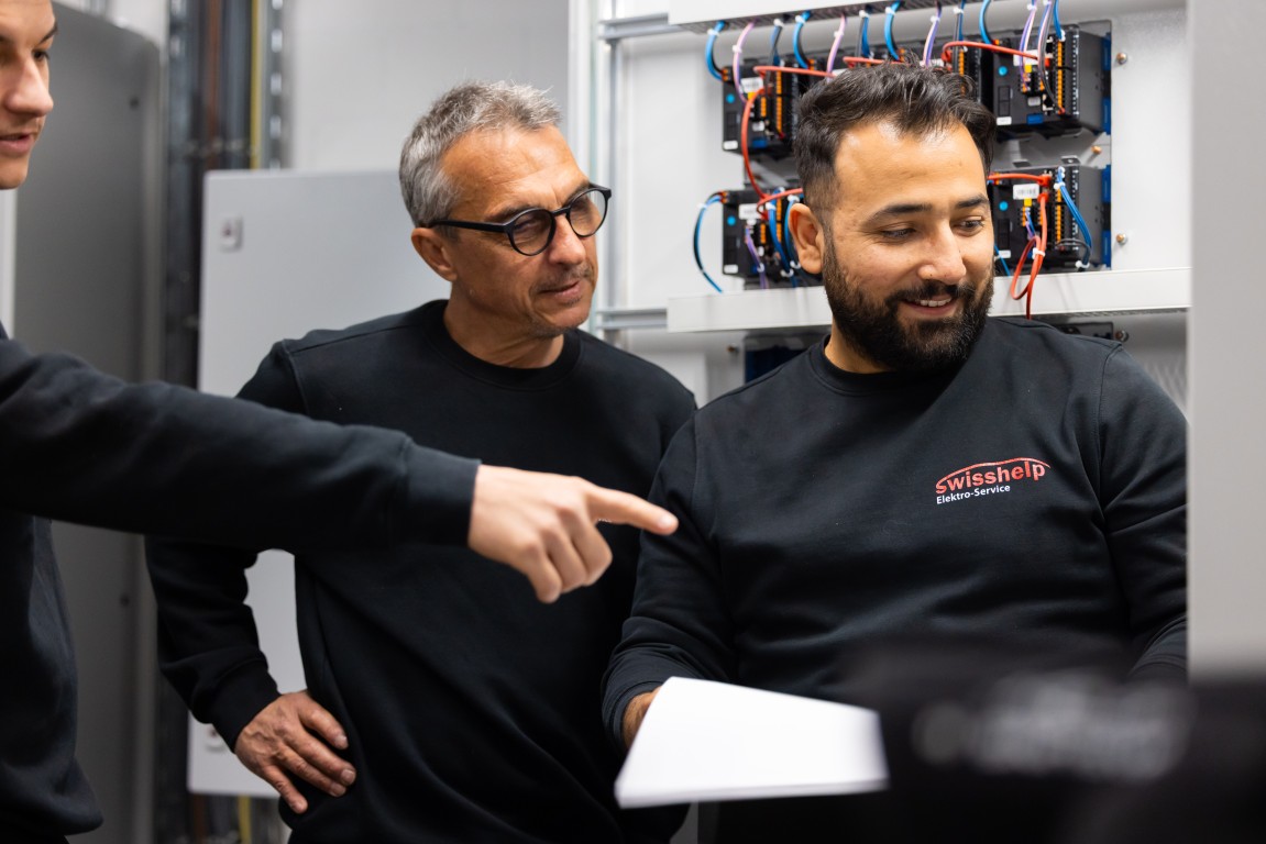 Zwei Monteure von Swisshelp Elektro besprechen eine Störung am offenen Schaltschrank