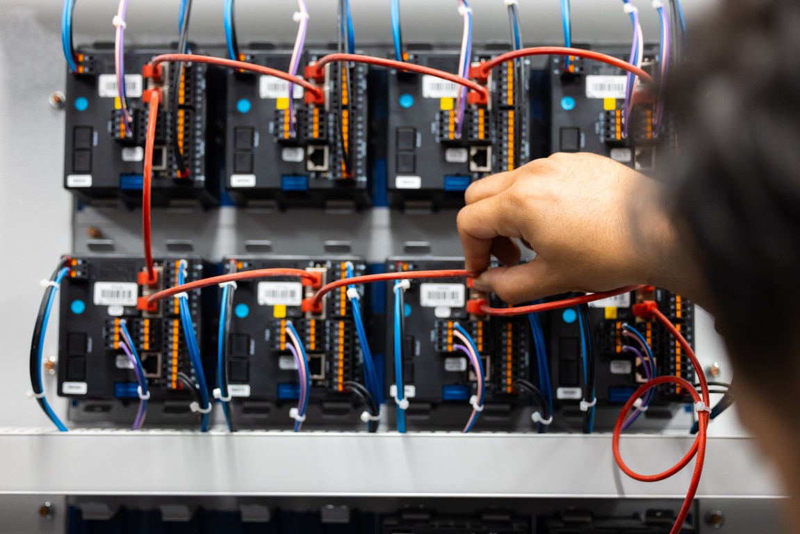 Hand steckt ein rotes Patchkabel in ein Netzwerkmodul im Schaltschrank